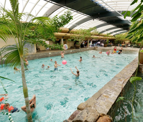 Overzicht van het golfslagbad in de Aqua Mundo van Center Parcs Het Meerdal, vol met families die spelen in het water onder de grote glazen koepel.