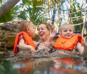 Een lachende moeder heeft plezier met haar twee jonge kinderen, die zwemvestjes dragen, in het water van de Aqua Mundo van Center Parcs Erperheide.