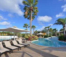 Het zwembad van CHOGOGO Dive & Beach Resort met luxe ligbedden, parasols en wuivende palmbomen.