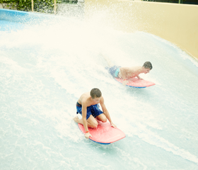 Twee jongens leren surfen op de Flow Rider surfsimulator in de Aqua Mundo van Center Parcs De Eemhof, liggend op hun bodyboards op de golf.
