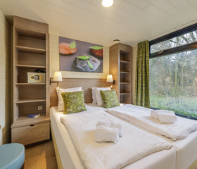 De comfortabele slaapkamer in een vernieuwde cottage bij Center Parcs De Huttenheugte, met opgemaakte bedden en een groot raam met uitzicht op de natuur.