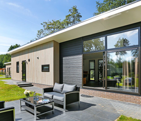 Zonnig en ruim terras van een moderne lodge op Vakantiepark De Lochemse Berg, met een comfortabele loungeset en uitzicht op de tuin.