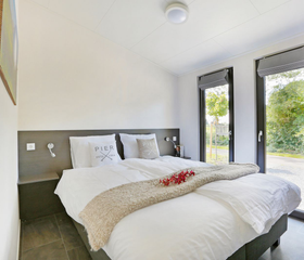 Comfortabele tweepersoons slaapkamer in een lodge op Vakantiepark De Lochemse Berg, met openslaande deuren naar de groene tuin