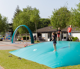 Kinderen die zich uitleven en hoog springen op de grote airtrampoline (luchtkussen) op RCN de Roggeberg, een populaire speelplek.
