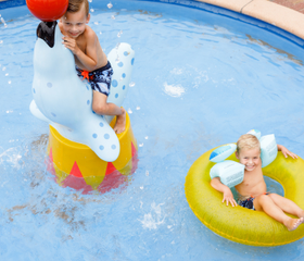 Twee jonge kinderen spelen in het verwarmde peuterbad van RCN de Schotsman, met een speelse zeehond en een zwemband.