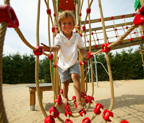Een jongen balanceert op een touwbrug in de avontuurlijke buitenspeeltuin met zand bij kindvriendelijk vakantiepark De Wije Werelt.