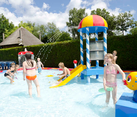 Kinderen spelen en spetteren in de waterspeeltuin 't Houtse Hoofd bij De Wije Werelt, met een glijbaan en watersproeiers voor waterpret.