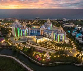 Het prachtig verlichte Delphin BE GRAND Resort in Lara bij zonsondergang, gezien vanuit de lucht.