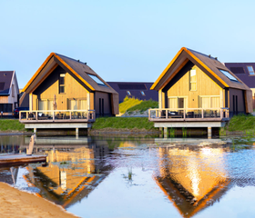 Twee luxe waterwoningen met een houten vlonderterras direct aan het water, weerspiegeld in het water op Dormio Resort Nieuwvliet-Bad.