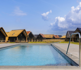 Het verwarmde buitenzwembad van Dormio Resort Nieuwvliet-Bad, omringd door luxe vakantiewoningen onder een helderblauwe lucht.