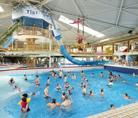 Overzicht van het drukke golfslagbad binnen in het Tikibad, waar veel gezinnen en kinderen genieten van de golven en het zwemmen.