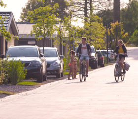 Een gezin fietst vrolijk door de straten van vakantiepark EuroParcs Markermeer, met jonge boompjes langs de weg.