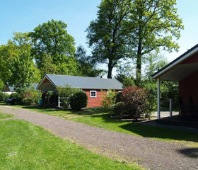 Een rood vakantiehuisje op een rustig pad omgeven door gras en bomen op EuroParcs Resort De Utrechtse Heuvelrug.