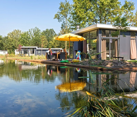 Moderne vakantiewoning met een vlonderterras en gele parasol, direct gelegen aan het water op EuroParcs Resort Limburg.