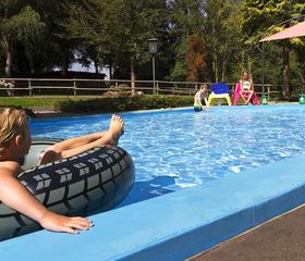 Een meisje relaxt in een grote zwemband in het verkoelende water van het buitenzwembad bij Feriendorf Felsenhof.