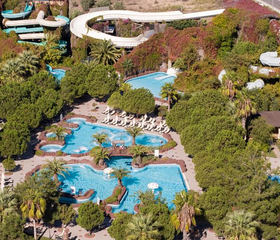 Overzicht van de prachtig aangelegde lagune-stijl zwembaden en waterglijbanen, omgeven door groene bomen bij Hotel Ali Bey Club.
