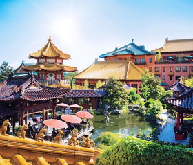 Zonnig aangezicht van Hotel Ling Bao bij Phantasialand, met de kenmerkende Chinese architectuur, daken en een terras aan het water.