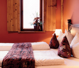 Sfeervol opgemaakt tweepersoonsbed in een familiekamer van Hotel Ling Bao, met decoratie in Aziatische stijl en warme, rode kleuren.