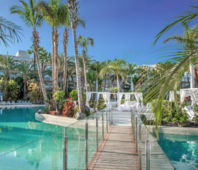 Het tropische zwemparadijs van Maspalomas Princess met een houten brug over het helderblauwe water en luxe witte cabana's.