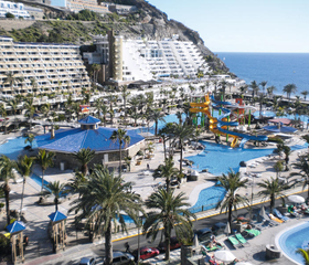 Overzicht van het grote waterpark Paradise Lago Taurito op Gran Canaria, met de vele zwembaden, glijbanen en het hotel tegen de heuvels aan de kust.