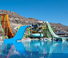 De hoge en kleurrijke waterglijbanen van het Aquapark Lago Taurito, met een brede blauwe en een steile oranje glijbaan die uitkomen in het zwembad.