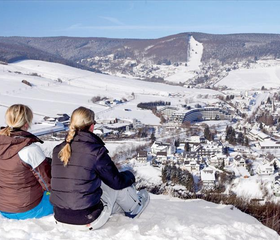 Twee wintersporters genieten van het panoramische uitzicht over het besneeuwde dorp Willingen vanaf de top van een berg in Sauerland.
