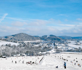 Weids overzicht van het kindvriendelijke skigebied van Willingen in Sauerland, met veel skiërs op de besneeuwde pistes onder een strakblauwe lucht.