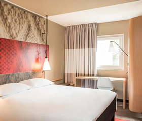 Een comfortabele en moderne hotelkamer in het Ibis Hotel in Aken, met een groot tweepersoonsbed en een rood hoofdeinde.