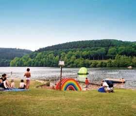 Gezinnen met kinderen genieten van de zon op het zandstrand aan de oever van de Kronenburger See, vlak bij het vakantiepark.