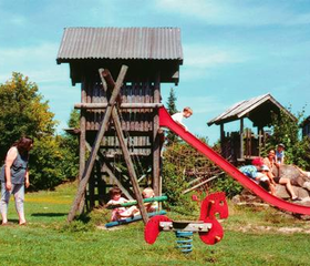 Kinderen spelen in de houten speeltuin met een grote glijbaan en klimtoren op vakantiepark Feriendorf Waldbrunn.