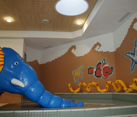 Het vrolijke kinderbad in Feriendorf Waldbrunn met een blauwe dolfijnenglijbaan en een mozaïek van een clownvis.