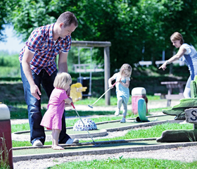 Gezin met jonge kinderen speelt een potje midgetgolf op de midgetgolfbaan van Vakantiepark Sandur.