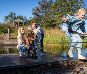 Gezin met kinderen en hond heeft plezier op een houten trekvlot bij het water op Kustpark Texel.