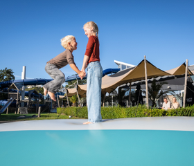 Twee kinderen springen hand in hand op de grote airtrampoline op Kustpark Texel.