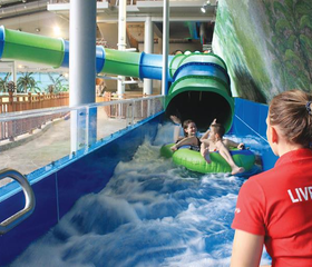 Kind op een mat in de Wild River glijbaan in het Aquadome waterpark van Lalandia Billund, onder toezicht van een badmeester.