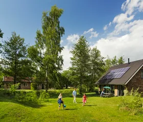 Kinderen spelen en rennen op een groot, groen grasveld voor een vrijstaande bungalow met zonnepanelen op vakantiepark Landal Aelderholt.