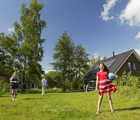 Drie kinderen spelen samen met een bal op een groot grasveld voor hun vakantiebungalow op een zonnige dag bij Landal Aelderholt.