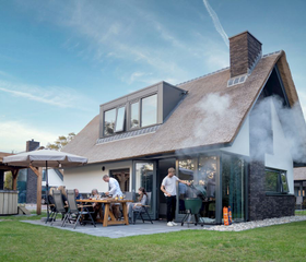Een gezin geniet van een barbecue op het overdekte terras van hun luxe vakantiehuis met rieten dak op Landal Berger Duinen.