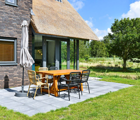 Het zonnige terras met een houten tuinset en parasol van een rietgedekte vakantievilla op Landal Berger Duinen.