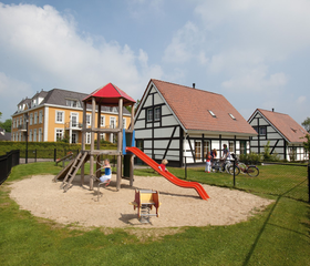 Een leuke speeltuin met een glijbaan en klimrek in een zandbak op het vakantiepark Landal Cauberg, gelegen tussen de vakwerkhuizen.
