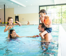 Ouders hebben plezier met hun kinderen op de schouders in het zwembad van Landal De Vers.
