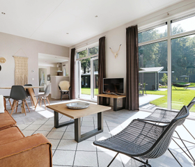 De lichte, moderne woonkamer van een lodge op Landal De Vlinderhoeve met grote ramen en openslaande deuren naar de tuin.