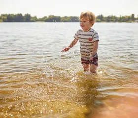 Een klein jongetje speelt en spettert in het ondiepe water van de Wedderplassen bij Landal.