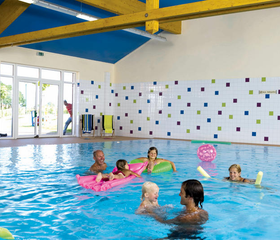 Kinderen en een baby spetteren en spelen vrolijk met speelmatten in het overdekte zwembad van Landal Dwergter Sand.