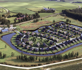 Luchtfoto van vakantiepark Landal Elfstedenhart, waarop de cirkelvormige opzet van de waterwoningen in het Friese landschap te zien is.
