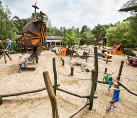 Overzicht van de grote avontuurlijke buitenspeeltuin van Landal Heideheuvel met zand, water en diverse speeltoestellen.