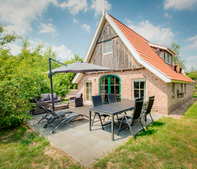 Een ruim, gemeubileerd terras met loungeset, eettafel en parasol bij een vrijstaande bungalow midden in het groen op Landal Hellendoornse Berg.