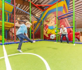 Twee jongens voetballen op het sportveldje in het kleurrijke indoorspeelparadijs van Landal Hochwald.