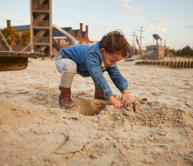 Een jonge jongen in een spijkerblouse is aan het graven en spelen in het zand van de grote avontuurlijke buitenspeeltuin op vakantieresort Landal Hof van Saksen.