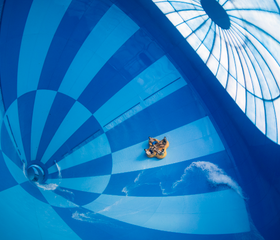 Een groep mensen in een gele opblaasbare band glijdt door de gigantische, blauw-wit geblokte trechter van de waterglijbaan Saltato in het zwemparadijs van Landal Hof van Saksen.